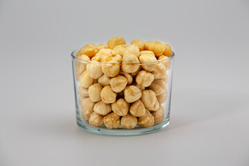 Pile of hazelnuts in glass bowl on white background.