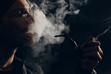 Fototapeta na wymiar Man smoking a pipe on dark background. Back lit profile portrait
