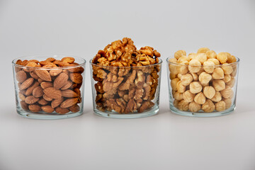 Pile of walnuts, almonds and hazelnuts in glass bowl on white background.