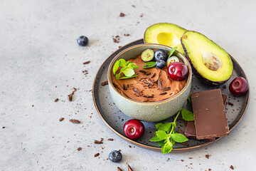 Raw avocado chocolate mousse topped with chocolate pieces, cherry, blueberry and mint, selective...