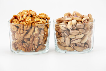 Pile of salted pistachios and walnuts  in glass bowl on white background.