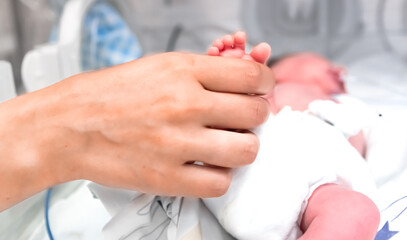 Nurse takes action to monitor and care for premature baby, selective focus - baby foot and nurse arm. Newborn is placed in the incubator. Neonatal intensive care unit