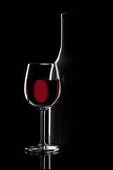 Glass of red wine next to a bottle backlit on a black background. 3d illustration.