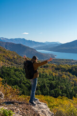 A traveler with a backpack stands on the top of the mountain and holds his hands to the sides