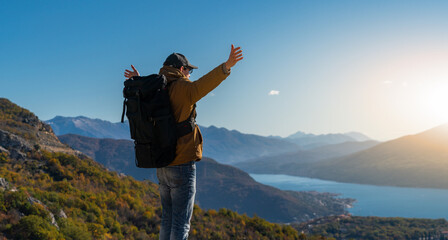 Obraz premium A traveler with a backpack stands on the top of the mountain and holds his hands to the sides