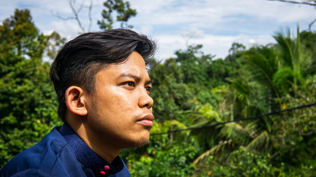 A Portrait Of A Malay Man Model Wearing A Blue Traditional Baju Melayu With Green Nature Background.