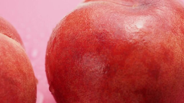 Wet peaches rotate on a pink background.