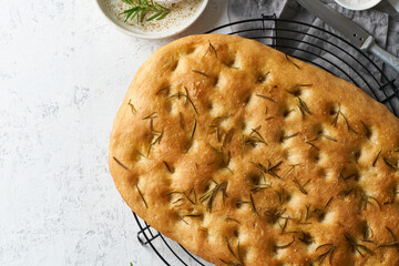 Focaccia, pizza, italian flat bread with rosemary and olive oil on grid on white rustic table, tradition italian cuisine, top view, copy space