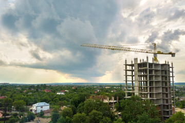 Fototapeta premium Aerial view of tower lifting crane and concrete frame of tall apartment residential building under construction in a city. Urban development and real estate growth concept.