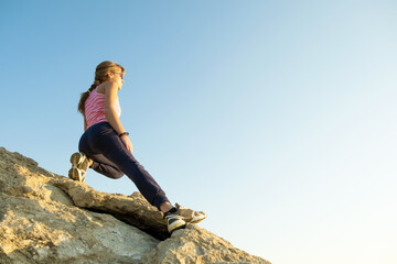 Obraz premium Woman hiker climbing steep big rock on a sunny day. Young female climber overcomes difficult climbing route. Active recreation in nature concept.