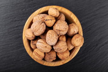Walnut in wooden bowl on black background with copy space.