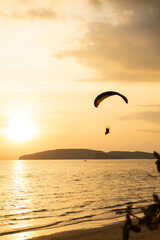 A paraglider swooping low over a Thai beach as the sun begins to set in the background