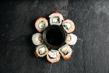 The range of different types of sushi, rolls and Maki with sauces and chopsticks. On black rustic background