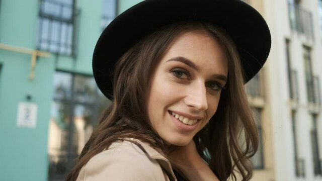 Portrait of a young female businesswoman in glasses, raincoat and hat with a sincere smile posing in front of the camera holding. Food package with vegetables and fruits in hands. Model