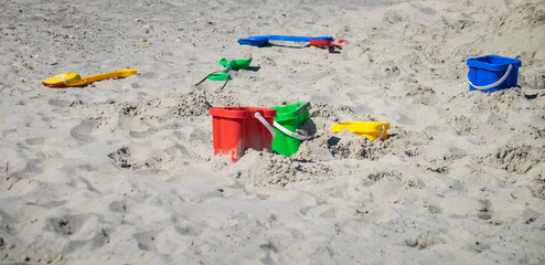 Colourful buckets and spades left laying on a sandy beach.