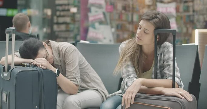 Mid-adult Caucasian woman yawning and putting head on travel bag as young female tourist sleeping on suitcase. Portrait of tired travelers waiting for departure in airport. Cinema 4k ProRes HQ.