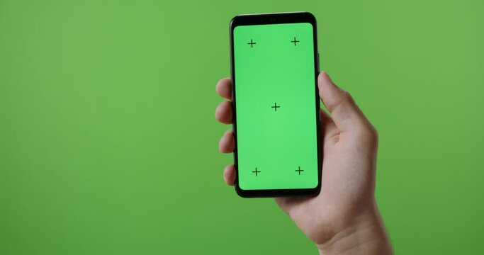 Hands of man holding a phone with vertical green chroma key screen. isolated on green background, swiping the touchscreen 4k template