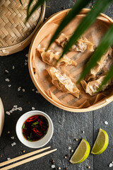 Gyoza dumplings with duck cooked in bamboo steamer on stone background served with soy sauce and cilantro. Top view, flat lay