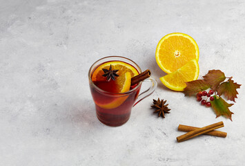Hot red autumn mulled wine in mug with spices and orange on grey background.