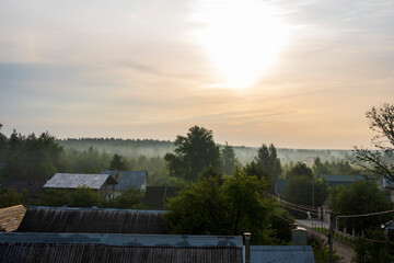 sunrise in the morning in a haze of fog over buildings, trees and fields