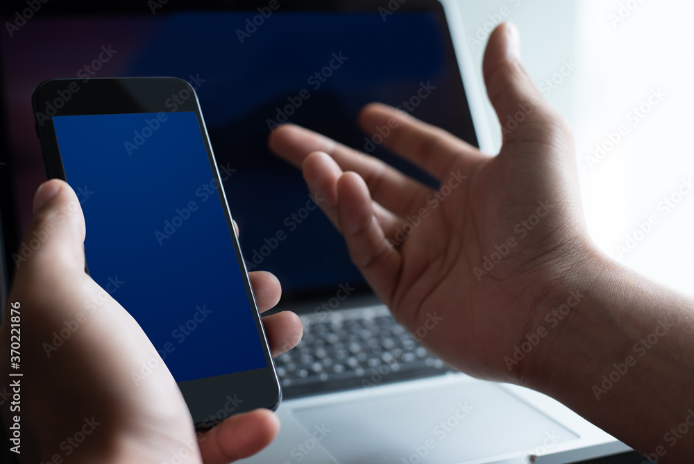 Poster mockup man using blue screen mobile smart phone while working on laptop computer at office