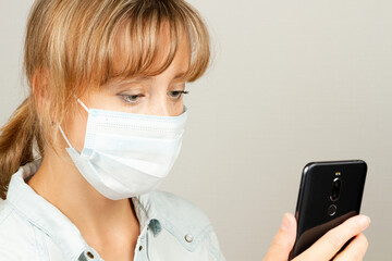a young girl during the coronavirus pandemic in a medical mask with a smartphone in her hands