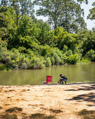 African American male calmly fishing from the bank of a lake, under a shade tree.