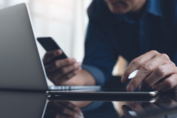 Multitasking business man working on digital tablet and laptop computer using mobile phone in office