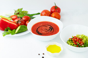 Ripe, bright vegetables-ingredients and cold gazpacho soup in a white Cup, on a white worn background. vegan and vegetarian food.