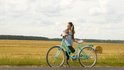 Fototapeta premium a pensive girl with a retro bike in the countryside stands on the side of the route and looks to the side. banner. active lifestyle. copy space. place for your text