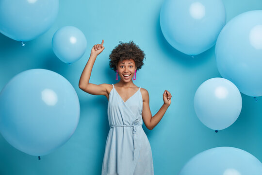 Upbeat cheerful festive woman with hollywood smile, laughs out of joy, moves carefree and dances to music, has fun, makes happy holiday photo, celebrates anniversary, surrounded by balloons.