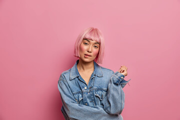 Serious fashionable young woman tilts head and bites lips, tries to think up solution, doubts about...