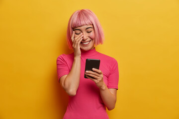 Overjoyed young Asian lady has bob hairstyle, laughs sincerely at message in social network, enjoys...