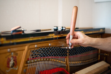 Technician, tuning a piano. Piano tuning is the act of adjusting the tension of the strings of an acoustic piano so that the musical intervals between strings are in tune. - obrazy, fototapety, plakaty