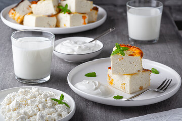 Cottage cheese casserole with raisins and cup of milk on wooden grey background. Cottage cheese casserole.