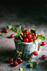 Naklejka na ściany i meble Fresh cherries with leaves and water droplets in a ceramic cup on a gray background.