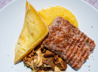 Traditional Italian mountain dish. Polenta, cheese, salami and mushrooms. Caloric and tasty dish. Plate of the Italian Alps and Dolomites