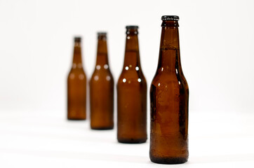 Four brown glass bottles of beer in line moving away from the first one on a white background.