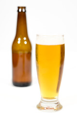 A beer glass filled with foam with a brown glass bottle to the side centered in the image with a white background.