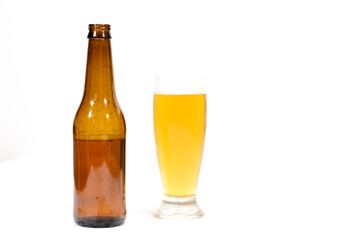 A beer glass filled with foam with a brown glass bottle to the side centered in the image with a white background.