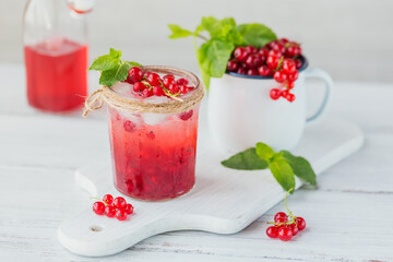 Glass of red currant cocktail or mocktail, refreshing summer drink with crushed ice and sparkling water on a white wooden background.
