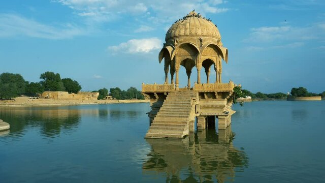 Structures made of yellow stone amidst water body, Gadisar lake in the beautiful city of Jaisalmer, artificially built for water conservation. Shot at Jaisalmer, Rajasthan, India. Blue sky background.