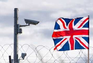 Flag of the United Kingdom  with surveillance camera and barbed wire, concept picture