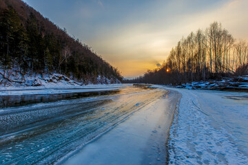 Obraz premium Northern landscape of Primorsky Territory, Samarga River. Frozen river in the taiga against the background of hills with coniferous trees at sunset