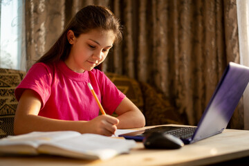 Fototapeta na wymiar Schoolgirl in pink t-shirt preparing homework at home in the evening