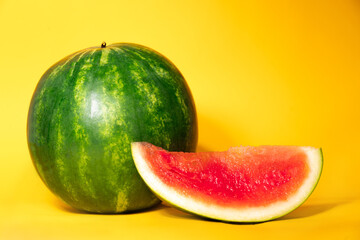 one whole watermelon and a slice of watermelon without seeds on a yellow background. summer theme. freshness. Refreshing juicy ripe delicious watermelon. august sweets.