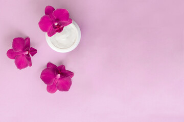 Obraz na płótnie Canvas White container with cream for face and body with three magenta colored orchid flowers on pink background. Concept of delicate or eco friendly cosmetics