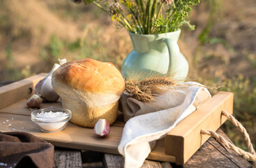 Still life of bread, wheat and garlic on a wooden box in natural conditions in nature. The concept of harvesting, farm products, natural food, cooking with your own hands, the unity of man with nature