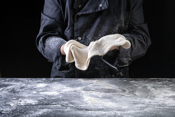 Chef making dough for pizza on dark backrground