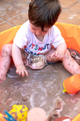 Child playing with sand in an orange plastic pool.